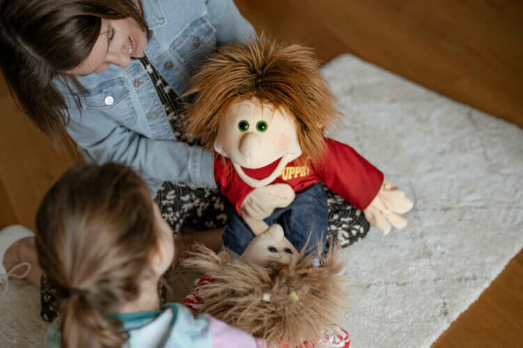 Julia Scherübl hält eine Puppe und unterhält sich mit einem Kind bei einer Therapiesitzung